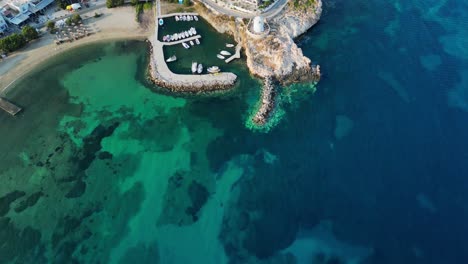 Aerial-footage-of-a-small-little-port-with-a-picturesque-windmill-in-the-town-of-Parikia,-on-the-island-of-Paros,-one-of-the-many-Cyclades-Islands-in-the-Aegean-Sea