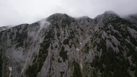 Misty-cliffs-of-Piatra-Craiului-Mountains-with-lingering-clouds,-aerial-view