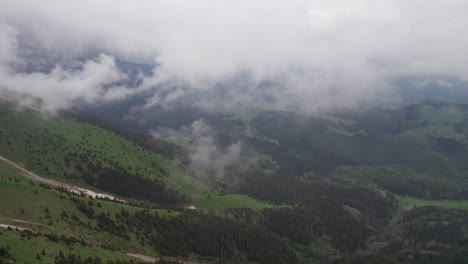 Misty-mountain-range-with-clouds-hovering-over-vibrant-green-slopes,-aerial-view