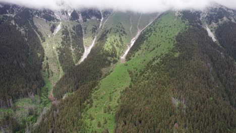 Lush-green-mountain-slopes-with-dense-forest-under-overcast-sky,-aerial-view