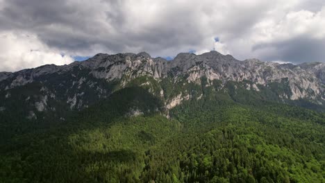 Lush-forest-at-the-base-of-the-towering-Piatra-Craiului-Mountains,-clouds-casting-shadows