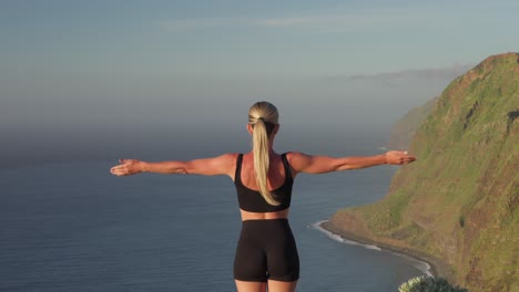 Yoga-Frau,-Die-Die-Arme-Zum-Himmel-Hebt-Und-Dabei-Auf-Die-Klippen-An-Der-Küste-Blickt