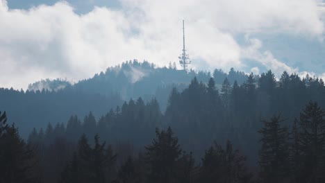 A-communication-tower-with-a-various-antennae-attached-stands-on-top-of-the-forest-covered-hill-in-the-Austrian-Alps