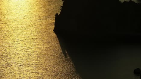 Golden-sunset-hues-over-the-Ionian-Sea-with-Corfu-Island-silhouette,-boat-shadow-on-water