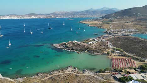 Aerial-footage-of-turquoise-waters-and-a-small-beach-club-on-the-island-of-Paros,-one-of-the-many-Cyclades-Islands-in-the-Aegean-Sea