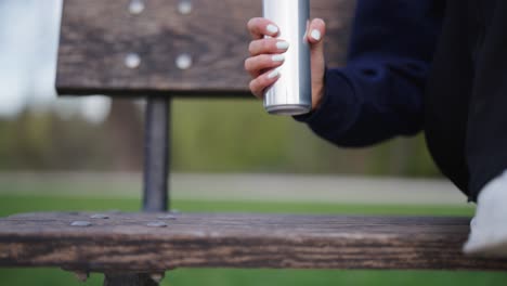 Woman-pick-up-shiny-aluminium-beverage-can-from-outdoor-wooden-bench
