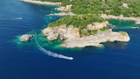 Speedboat-cutting-through-azure-waters-near-the-lush-cliffs-of-Corfu-Island,-aerial-view