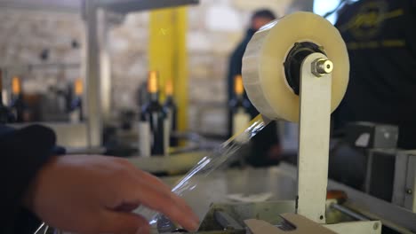 Wine-production-line-with-plastic-neck-cover-machine-and-bottles-in-conveyor-belt-with-workers,-Close-up-shot