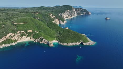 Corfu-island-coastline,-clear-blue-ionian-sea-waters,-lush-greenery,-sunny-day,-aerial-view