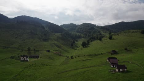 Aerial-shot-over-Sirnea-Village,-showcasing-cozy-houses-amid-lush-green-hills-under-a-cloudy-sky