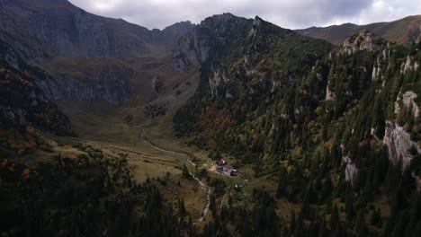 Autumn-colors-dress-the-Bucegi-mountains,-remote-chalet-nestled-in-the-valley,-aerial-shot