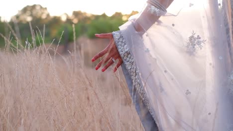 Cropped-View-Of-An-Indian-Bride-In-Nature-Touching-Golden-Grass-Fields-At-Sunset
