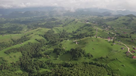Lush-green-hills-with-scattered-houses,-under-a-cloudy-sky,-aerial-view