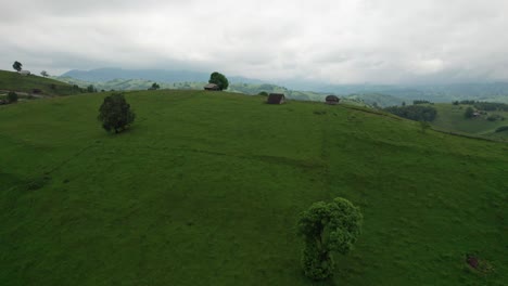 Aerial-shot-of-a-quaint-village-with-scattered-houses-amidst-green-hills,-under-overcast-skies,-daytime
