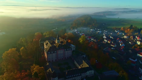 Aerial-view-tilting-toward-the-Schloss-Birstein-castle,-hazy-sunrise-in-Germany