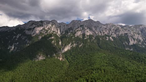 Majestic-Piatra-Craiului-Mountains-with-lush-forest-under-cloudy-skies,-aerial-shot