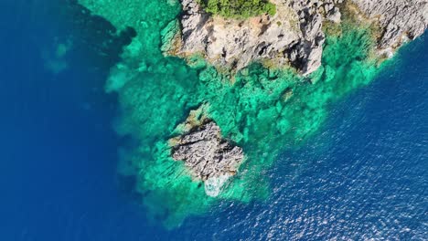 Acantilados-Iluminados-Por-El-Sol-En-La-Isla-De-Corfú-En-El-Mar-Jónico,-Mostrando-Vibrantes-Aguas-Azules,-Vista-Aérea