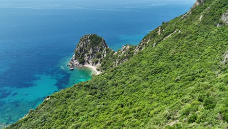 Lush-green-cliffs-overlooking-the-clear-blue-waters-of-the-Ionian-Sea-on-Corfu-Island,-Greece,-aerial-view