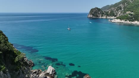 A-sailboat-on-clear-blue-waters-near-corfu-island-coast,-sunny-day,-aerial-view