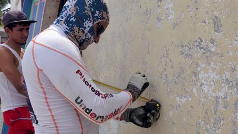 Jóvenes-Trabajadores-Latinos-Que-Trabajan-Reparando-Casas-Rurales,-Miden-La-Pared-Para-Poner-Un-Marco-De-Madera.