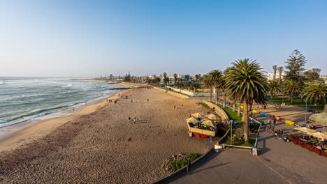 Swakopmund-beach-and-boardwalk-in-Namibia,-featuring-palm-trees-and-people-enjoying-a-sunny-day