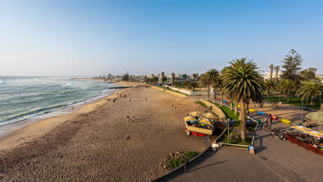 Playa-Y-Paseo-Marítimo-De-Swakopmund-En-Namibia,-Con-Palmeras-Y-Gente-Disfrutando-De-Un-Día-Soleado