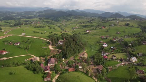 A-quaint-village-with-a-church-surrounded-by-lush-greenery-and-rolling-hills,-aerial-view