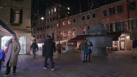 Festliche-Lichter-Erhellen-Einen-Lebhaften-Venezianischen-Platz-Und-Werfen-Einen-Warmen-Schein-Auf-Eine-Geschäftige-Abendszene