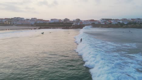 Luftaufnahme-Eines-Surfers,-Der-Während-Des-Sonnenuntergangs-Am-Strand-Von-Baleal,-Portugal,-Auf-Einer-Welle-Zwischen-Einer-Surfergruppe-Im-Atlantik-Surft