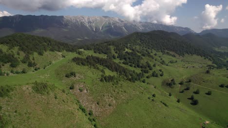 Verdant-alpine-landscape-with-Piatra-Craiului-Mountains-backdrop,-sunny-day,-aerial-view
