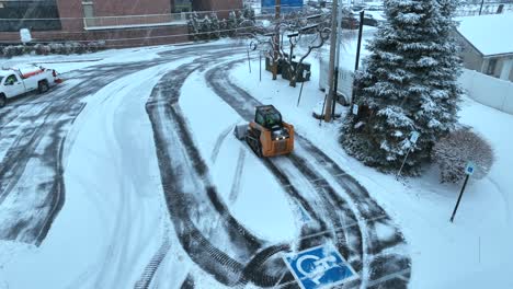 Skid-steer-loader-and-truck-with-plow-removing-snow-from-parking-lot-during-winter-blizzard-in-American-town