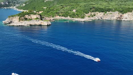 A-boat-cruising-near-the-rocky-shores-of-corfu-island,-greece,-on-the-ionian-sea,-sunny-day,-aerial-view