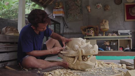 Male-Wood-Carver-Working-On-Traditional-Balinese-Barong-Mask-In-Bali,-Indonesia---Wide-Shot