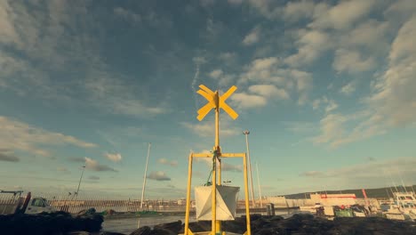 A-yellow-navigation-buoy-stands-proudly-on-the-dock-of-a-Spanish-coastal-fishing-village,-symbolizing-maritime-safety-and-guidance-amidst-the-bustling-activities-of-the-port