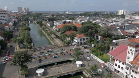 El-Tráfico-Fluye-Sobre-El-Canal-Alimentado-Por-El-Océano,-Cerca-De-Edificios-Históricos-De-La-Antigua-Batavia-Yakarta.