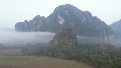 drone-shot-flying-towards-cliffs-shrouded-in-fog-in-Vang-Vieng,-the-adventure-capital-of-Laos