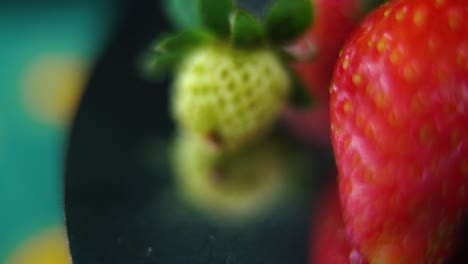 Macro-detailed-video-of-a-red-pile-of-strawberries,-tiny-green-RAW-strawberry,-on-a-rotating-stand,-smooth-movement,-slow-motion-120fps