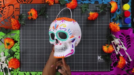 Hands-holding-colorful-Day-of-the-Dead-skull-decoration-on-vibrant-background,-top-view