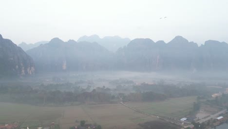 drone-shot-of-mist-in-the-valley-in-Vang-Vieng,-the-adventure-capital-of-Laos