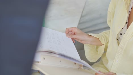 Una-Mujer-Sentada-En-Una-Mesa-En-La-Sala-De-Estar-Con-Su-Libro-Y-Bebida,-Primer-Plano,-Plano-Alto