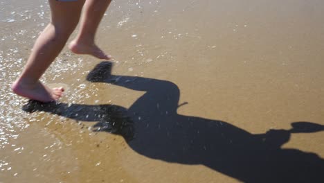 Nahaufnahme-Der-Füße-Eines-Dreijährigen-Jungen,-Der-In-Zeitlupe-Am-Strand-Entlangläuft-Und-In-Den-Wellen-Planscht