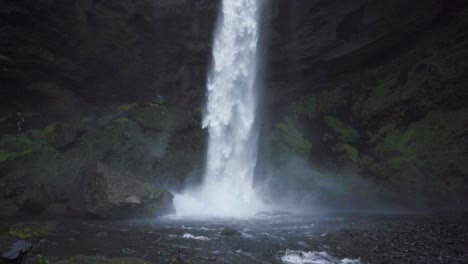 A-waterfall-in-Iceland,-surrounded-by-tall-cliffs-and-crashing-onto-rocks--Slow-motion