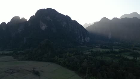 drone-shot-of-sun-rising-behind-mountains-in-Vang-Vieng,-the-adventure-capital-of-Laos