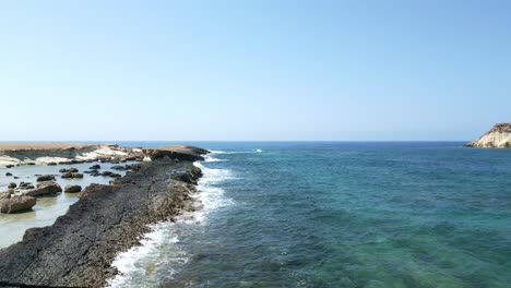 Rocky-coast-of-Agios-Georgios-Beach-in-Cyprus-with-clear-blue-waters-and-sunny-skies,-wide-shot