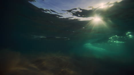 Underwater-view-of-longboarder-paddling-over-crashing-wave-at-sunrise