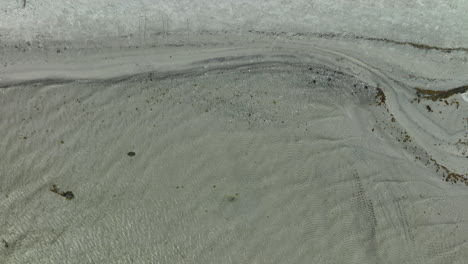 top-down-aerial-view-of-a-snowy-beach-beside-a-sea