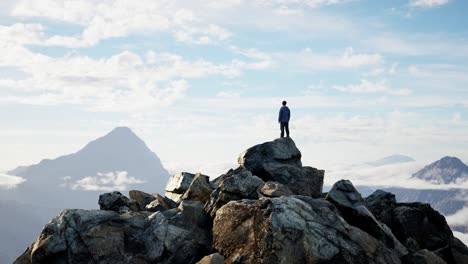 Adventurous-Male-Hiker-Standing-on-Rocky-Cliff-surrounded-by-Mountains