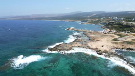 Agios-georgios-beach-in-cyprus-with-clear-blue-waters-and-windsurfers,-aerial-view
