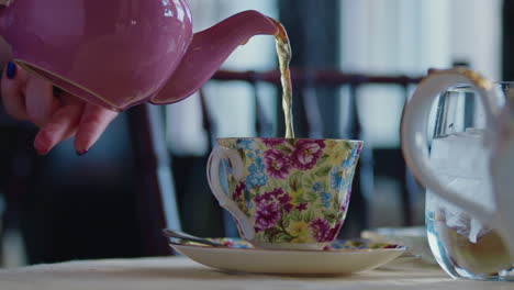 Nahaufnahme-Einer-Rosa-Teekanne,-Die-Tee-In-Eine-Geblümte-Tasse-Gießt