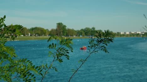 Serene-waters-of-Jarun-Lake-framed-by-verdant-foliage,-with-distant-paddlers-in-Zagreb,-Croatia